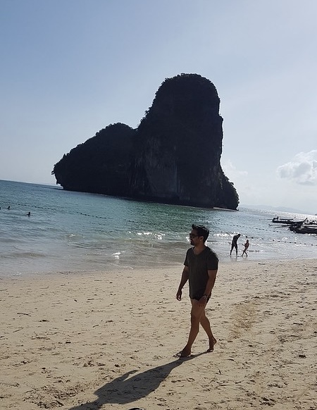 Sam Bhandari walking on a beach in Thailand with limestone cliffs in the background